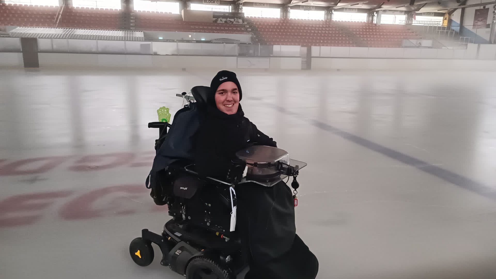 Joshua steht mit einem E-Rolli auf einer Eisfläche und lächelt in die Kamera. 