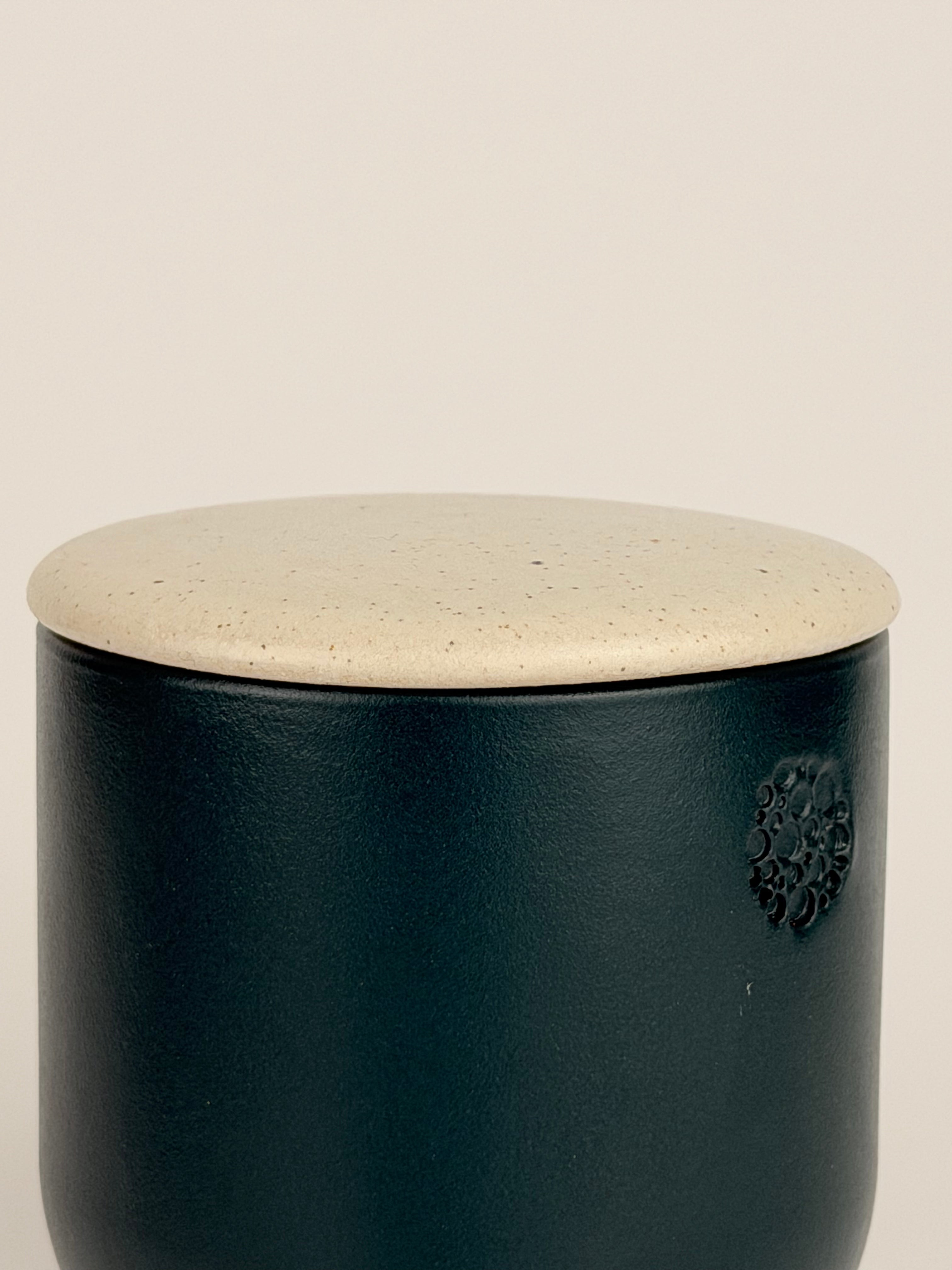 Dunkelgrüner (deep ivy) Keramikbehälter mit matter Oberfläche und eingeprägtem incalor Logo, darauf ein heller, gesprenkelter Deckel in Beige (sahara); vor neutralem Hintergrund fotografiert.