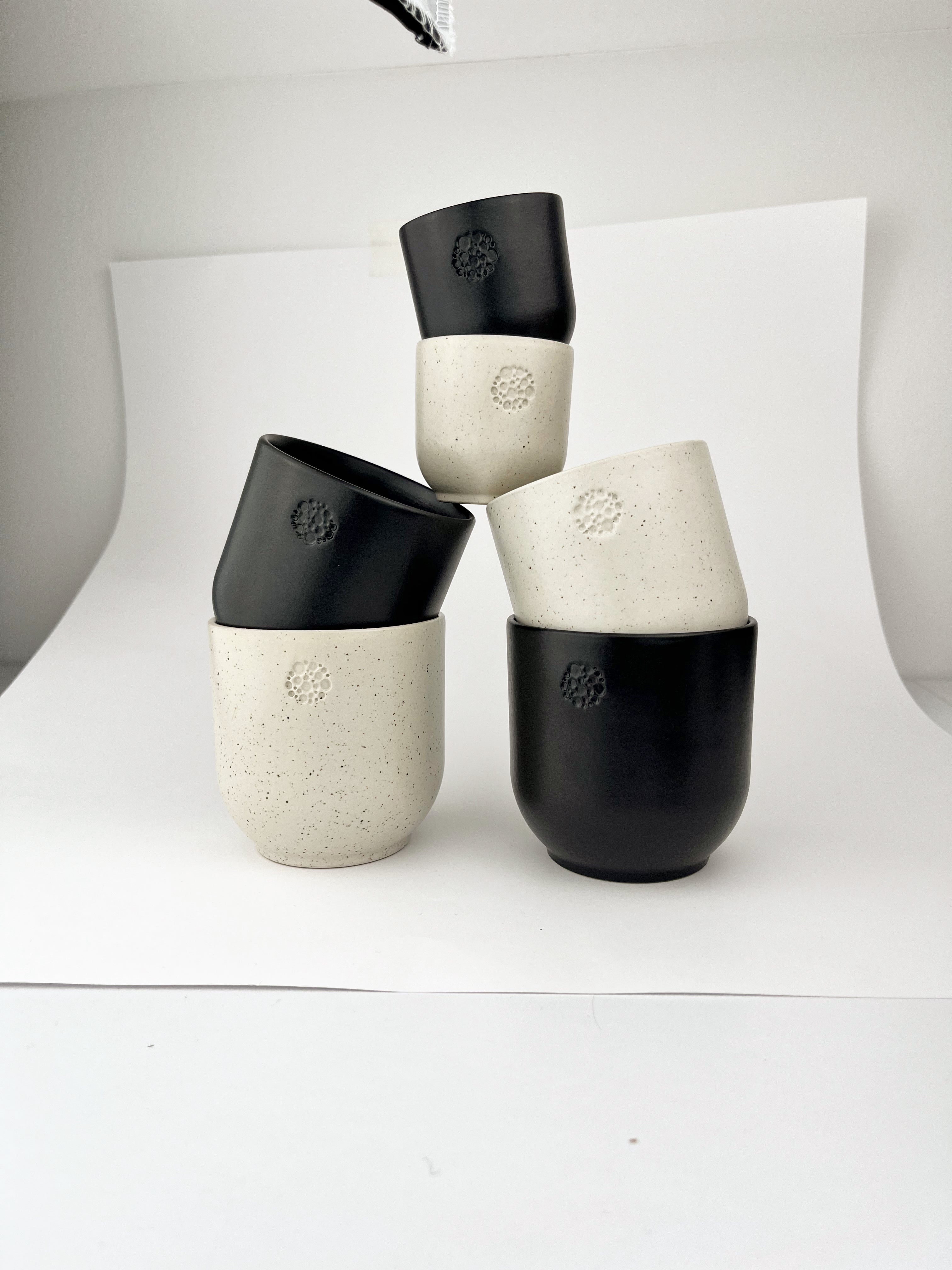Keramikbecher in den Farben basalt und sahara, verschiedene Größen, gestapelt vor einem weißen Hintergrund.