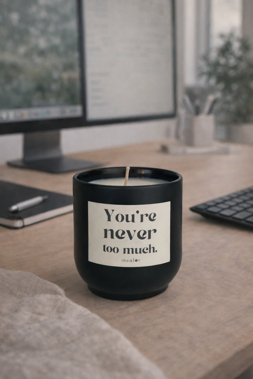 Dunkelgrüne (deep ivy) Kerze mit der Aufschrift ‚You’re never too much.‘ steht auf einem Schreibtisch. Im Hintergrund sind ein Computerbildschirm, Tastatur und Notizbuch zu sehen, was eine ruhige, moderne Arbeitsatmosphäre vermittelt.