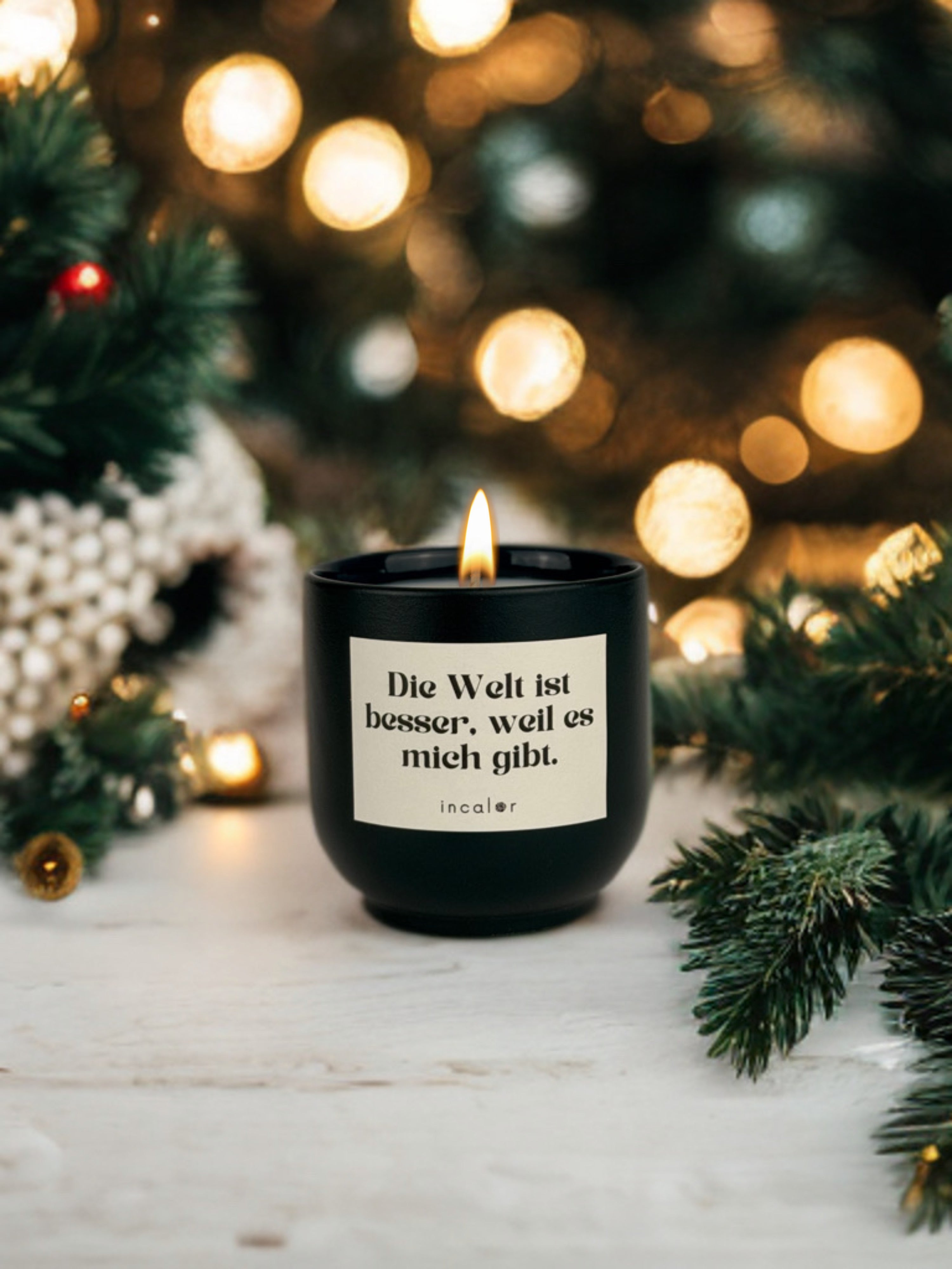 Dunkelgrüne (deep ivy) Duftkerze mit brennender Flamme steht auf einem hellen Untergrund, umrahmt von Tannenzweigen und weihnachtlicher Dekoration. Auf dem Etikett steht „Die Welt ist besser, weil es mich gibt.“ mit dem Markennamen „incalor“. Im Hintergrund leuchten unscharfe, warme Weihnachtslichter und erzeugen eine festliche Atmosphäre.