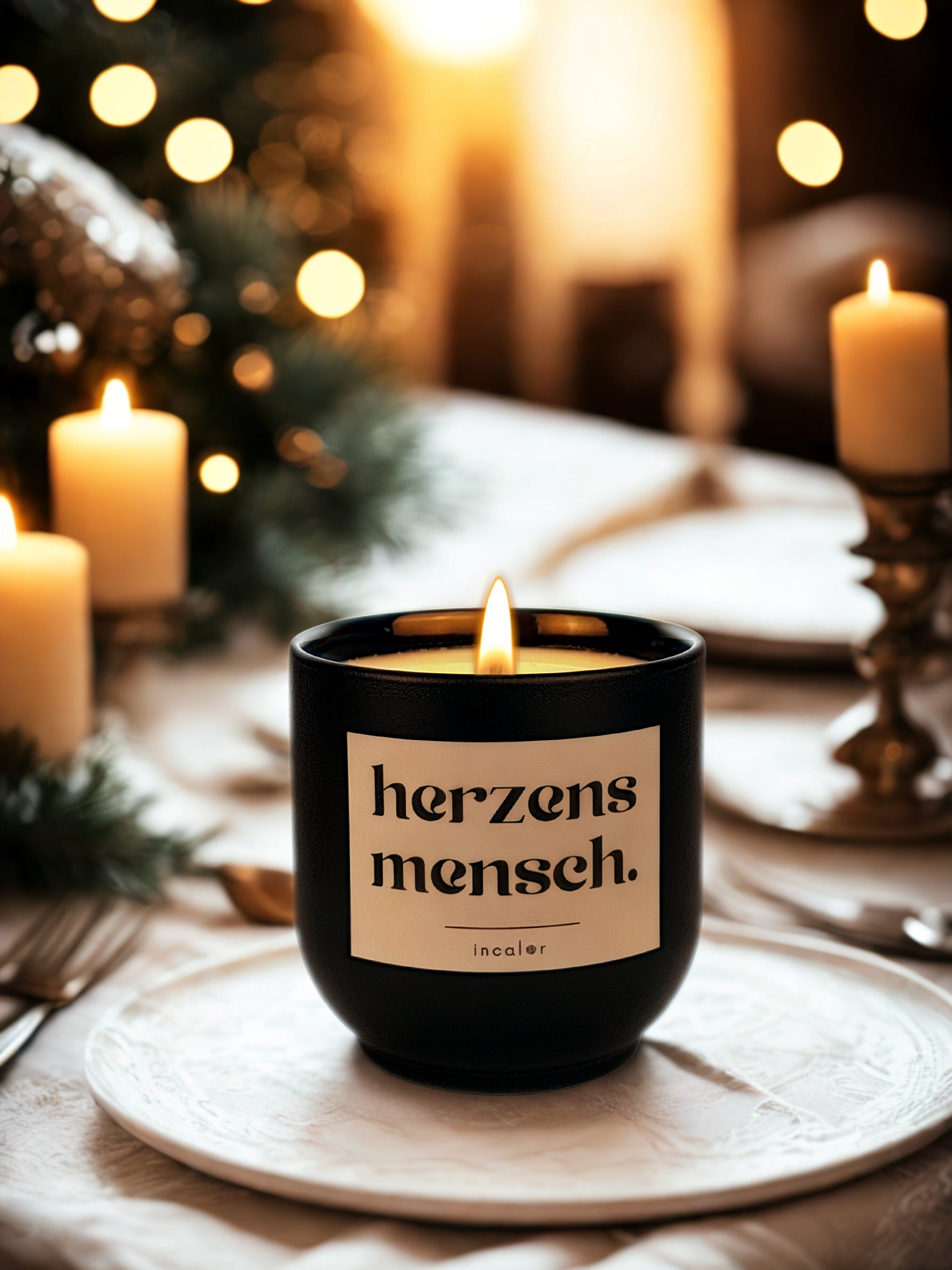 Dunkelgrüne (deep ivy) Duftkerze mit brennender Flamme steht auf einem festlich gedeckten Tisch. Auf dem Etikett steht „herzens mensch.“ mit dem Markennamen „incalor“ darunter. Im Hintergrund sorgen Kerzen, weiche Lichter und weihnachtliche Dekoration für eine warme, gemütliche Atmosphäre.