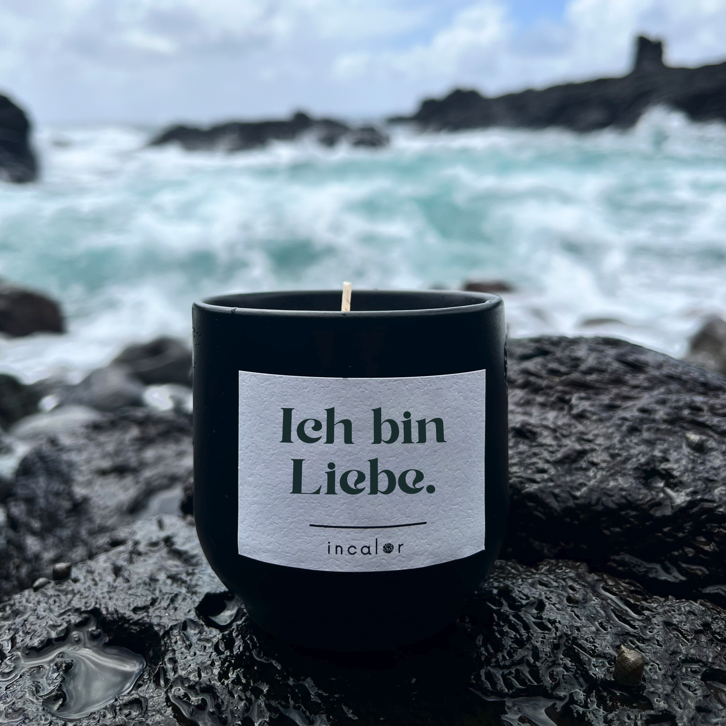 Schwarze Kerze aus Keramik (Farbton Basalt) mit Affirmation „Ich bin Liebe.“ von incalor, stehend auf feuchtem Lavagestein mit kraftvollen Meereswellen und dramatischer Küstenkulisse im Hintergrund – inspiriert von Selbstliebe und innerem Frieden.