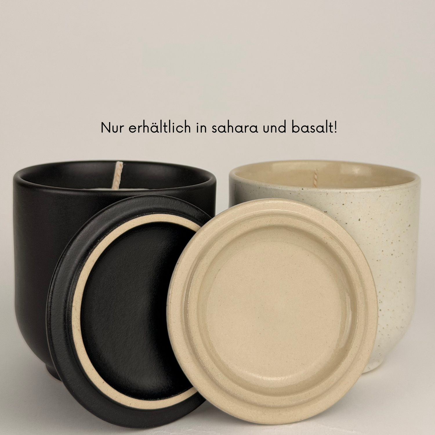 Zwei Kerzengefäße aus Keramik in den Farben Schwarz („basalt“) und Beige („sahara“) stehen nebeneinander. Davor liegen zwei passende Deckel in den gleichen Farben. Über den Gefäßen steht der Text: „Nur erhältlich in sahara und basalt!“.