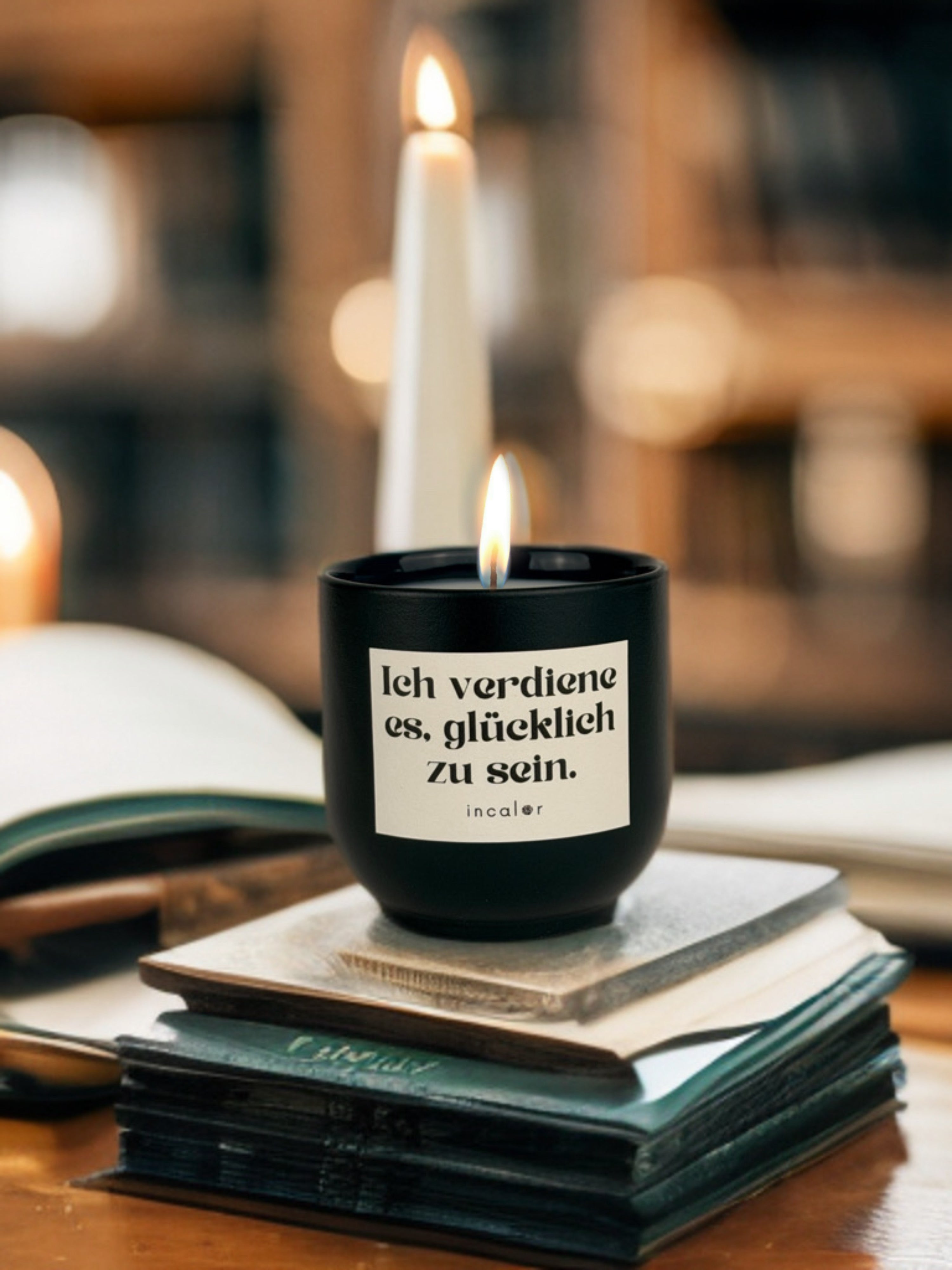 Dunkelgrüne (deep ivy) Duftkerze mit brennender Flamme steht auf einem Stapel geschlossener Bücher. Auf dem Etikett steht „Ich verdiene es, glücklich zu sein.“ und darunter der Markenname „incalor“. Im Hintergrund sind unscharfe Bücherregale und eine brennende Stabkerze zu sehen, was eine warme, inspirierende Atmosphäre erzeugt.